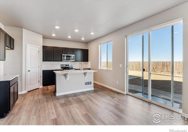 kitchen with appliances with stainless steel finishes, sink, decorative backsplash, a kitchen island with sink, and light hardwood / wood-style floors