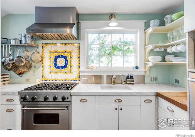 kitchen with sink, ventilation hood, light stone countertops, high end stove, and white cabinets