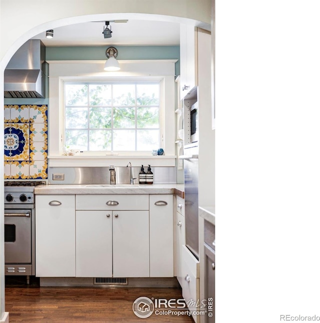 kitchen with wall chimney exhaust hood, sink, dark hardwood / wood-style flooring, high end stove, and white cabinets