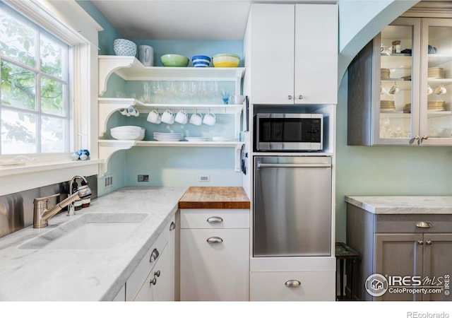 kitchen featuring stainless steel microwave, sink, light stone countertops, and white cabinets