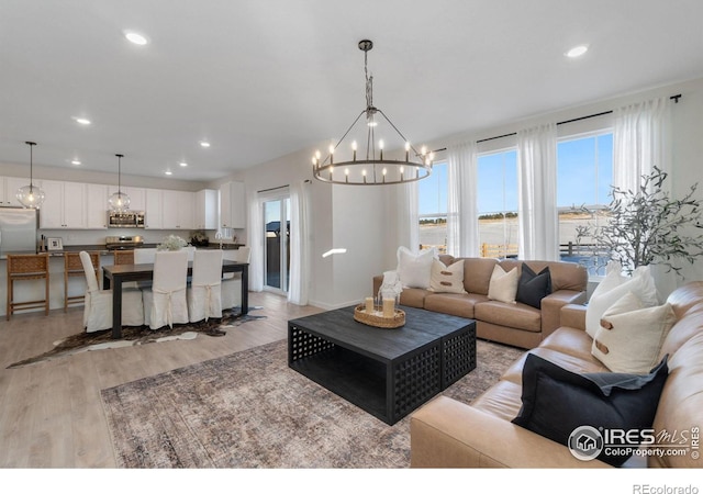 living room with a water view, a notable chandelier, plenty of natural light, and light wood-type flooring