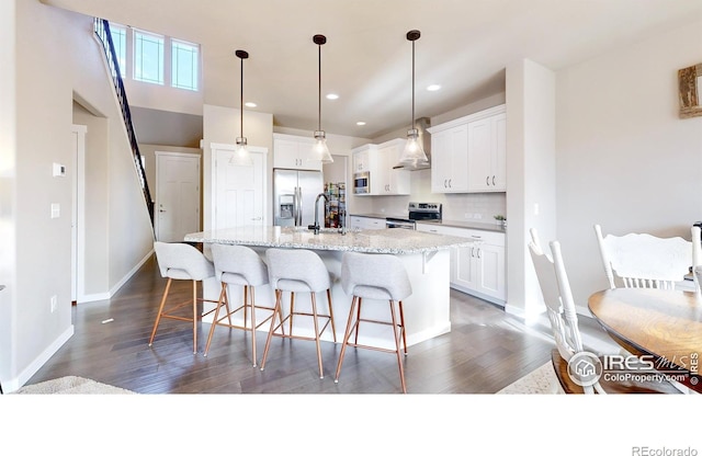 kitchen with stainless steel appliances, a center island with sink, pendant lighting, and white cabinets