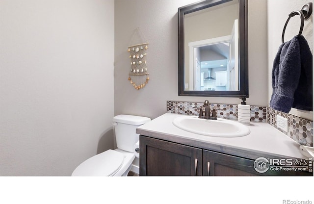 half bath with backsplash, vanity, and toilet