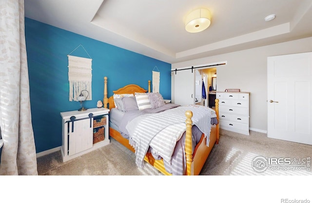 carpeted bedroom with a tray ceiling, baseboards, and a barn door