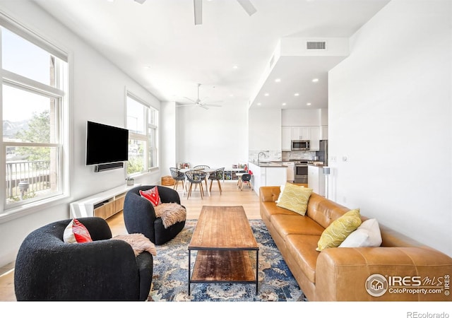 living room with light wood-type flooring, sink, and ceiling fan