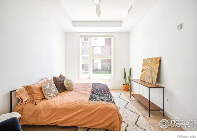 bedroom with ceiling fan, a raised ceiling, and light hardwood / wood-style flooring