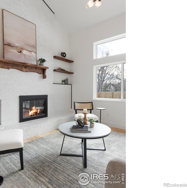 living room featuring high vaulted ceiling, a brick fireplace, and hardwood / wood-style floors