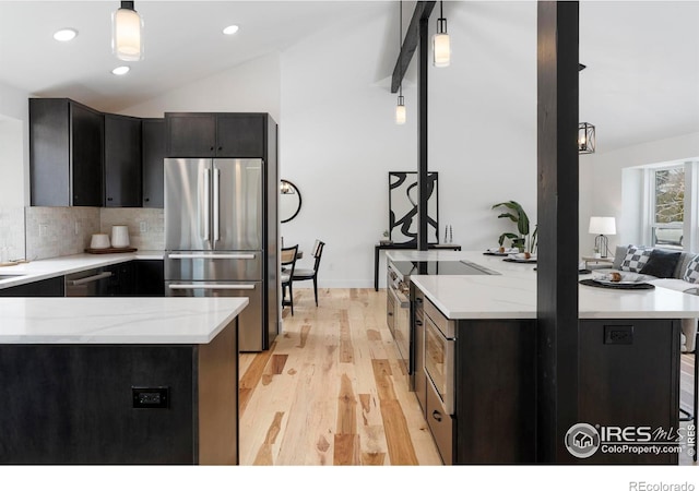 kitchen featuring vaulted ceiling, light stone counters, pendant lighting, a kitchen breakfast bar, and stainless steel appliances