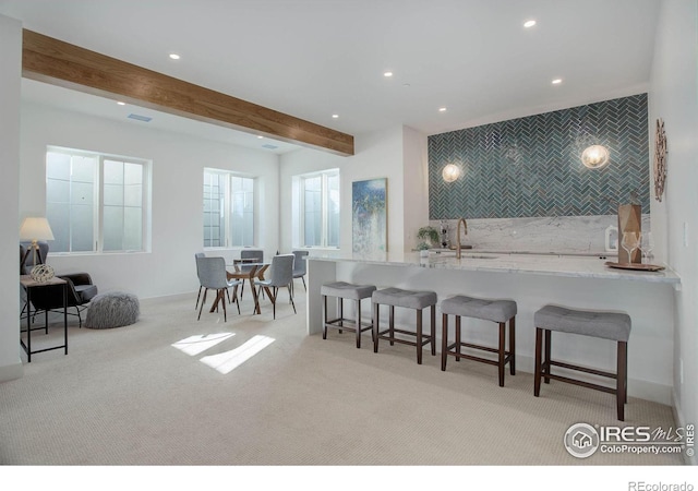 kitchen with a breakfast bar, beamed ceiling, sink, decorative backsplash, and light stone counters