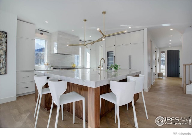 kitchen featuring sink, white cabinetry, decorative light fixtures, light hardwood / wood-style flooring, and a large island with sink