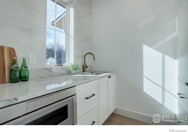 kitchen featuring stainless steel microwave, white cabinetry, sink, light stone counters, and light wood-type flooring