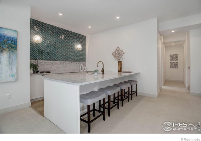 kitchen featuring a kitchen breakfast bar, light stone counters, tasteful backsplash, white cabinets, and kitchen peninsula