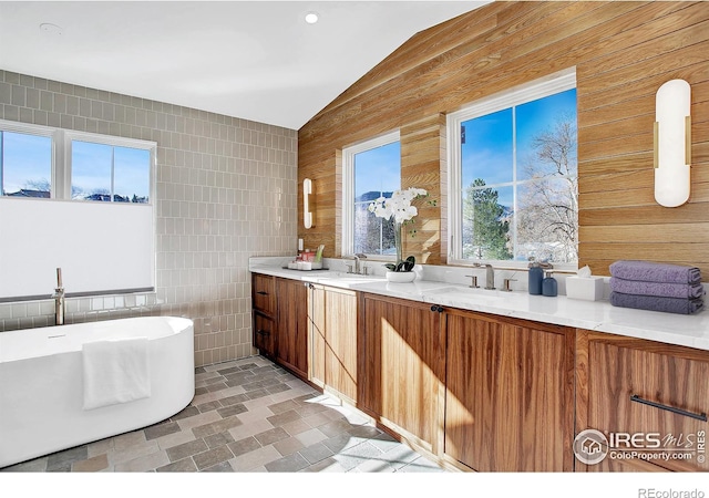 bathroom with a washtub, vanity, lofted ceiling, and tile walls