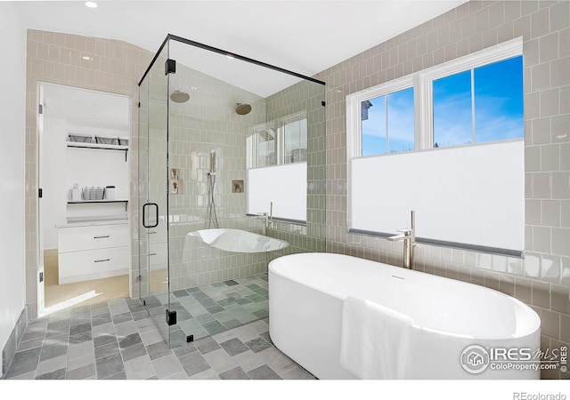 bathroom with shower with separate bathtub, vaulted ceiling, and tile walls