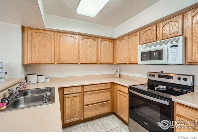 kitchen with stainless steel electric range oven, sink, light tile patterned floors, light brown cabinets, and a textured ceiling