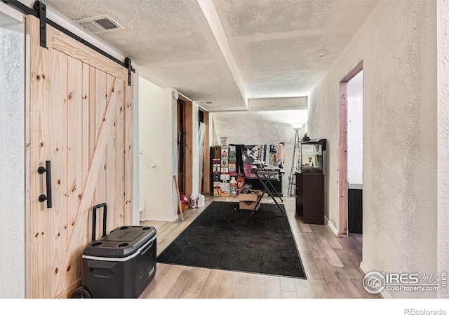 corridor featuring a barn door, light hardwood / wood-style flooring, and a textured ceiling