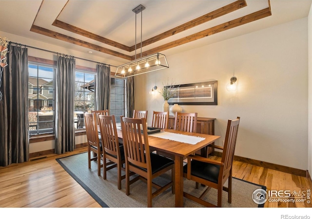 dining space with a raised ceiling and light hardwood / wood-style floors