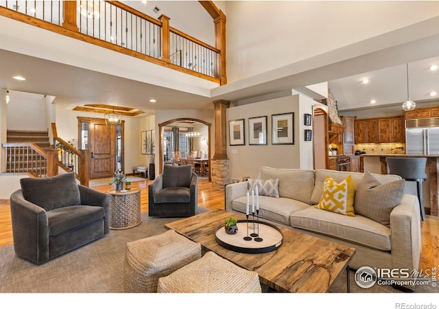 living room with an inviting chandelier, a towering ceiling, light hardwood / wood-style floors, and ornate columns