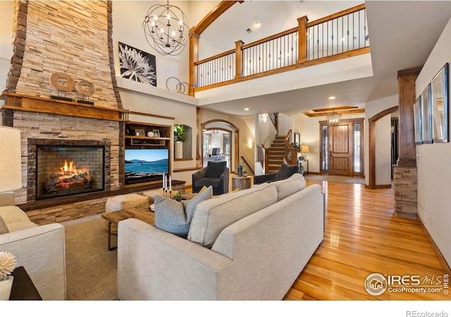 living room with an inviting chandelier, a stone fireplace, and light hardwood / wood-style flooring