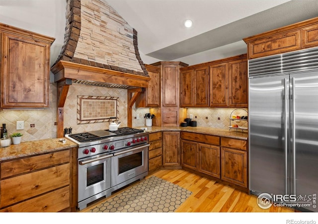 kitchen featuring lofted ceiling, high end appliances, light hardwood / wood-style flooring, custom range hood, and backsplash