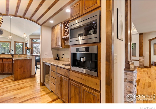 kitchen with vaulted ceiling, sink, hanging light fixtures, light hardwood / wood-style floors, and stainless steel appliances