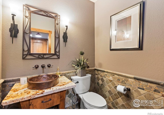 bathroom with vanity, toilet, and tile walls