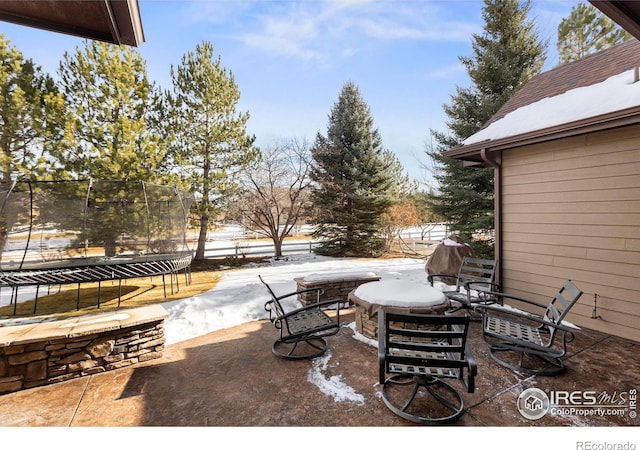 snow covered patio featuring an outdoor fire pit and a trampoline