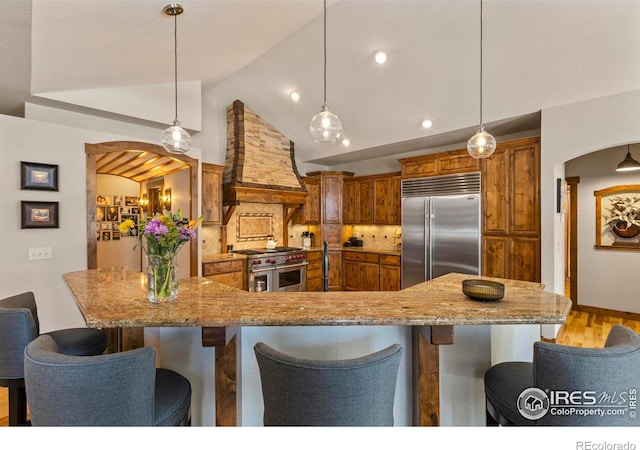 kitchen with high end appliances, decorative light fixtures, custom exhaust hood, and a breakfast bar area