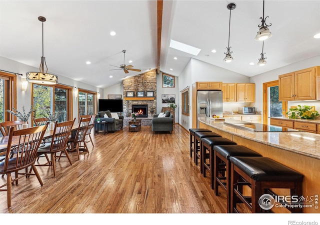 kitchen featuring appliances with stainless steel finishes, decorative light fixtures, a kitchen breakfast bar, light hardwood / wood-style floors, and light stone countertops