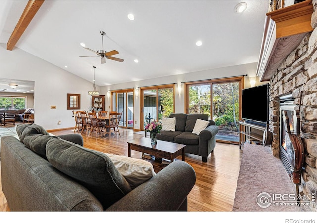 living room featuring beamed ceiling, plenty of natural light, a stone fireplace, and light hardwood / wood-style flooring