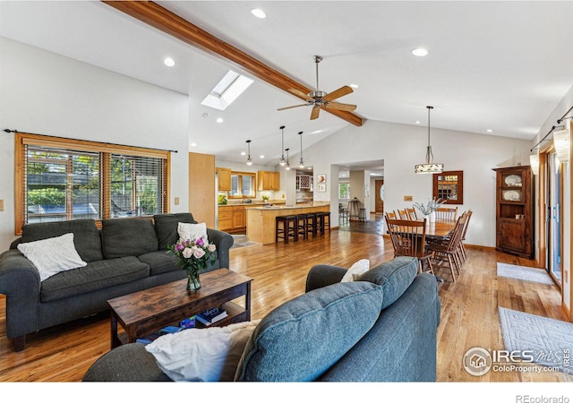 living room featuring high vaulted ceiling, a skylight, ceiling fan, light hardwood / wood-style floors, and beam ceiling