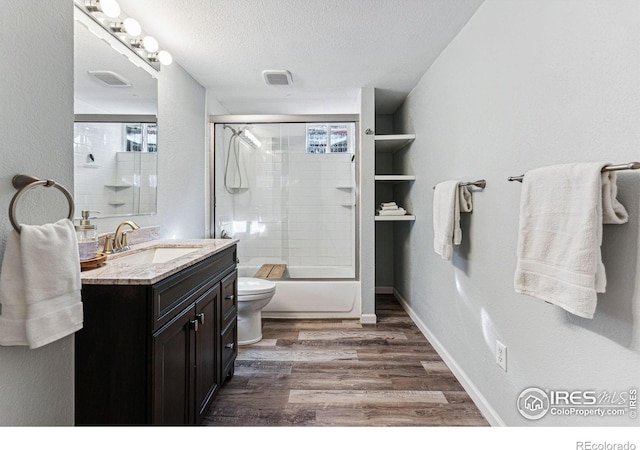 full bathroom featuring combined bath / shower with glass door, hardwood / wood-style flooring, vanity, toilet, and a textured ceiling