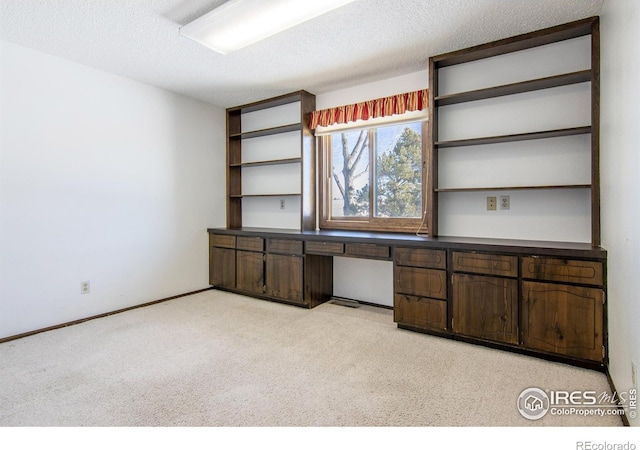 unfurnished office with light carpet, built in desk, and a textured ceiling