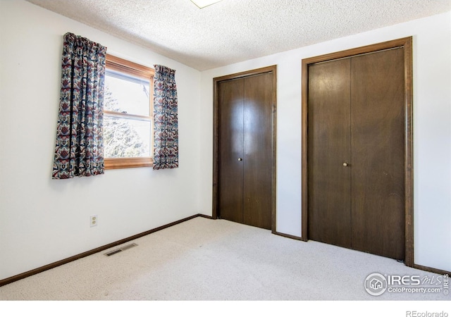 unfurnished bedroom featuring multiple closets, carpet, and a textured ceiling