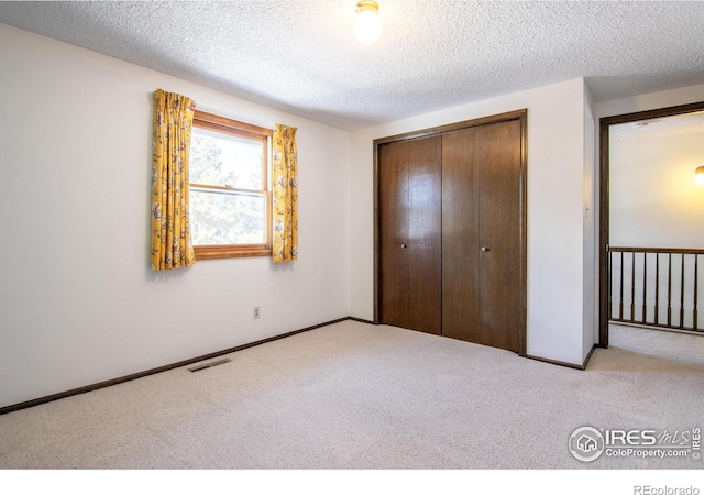 unfurnished bedroom featuring light carpet, a closet, and a textured ceiling