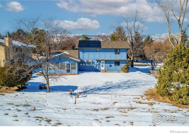 snow covered house with a mountain view and solar panels