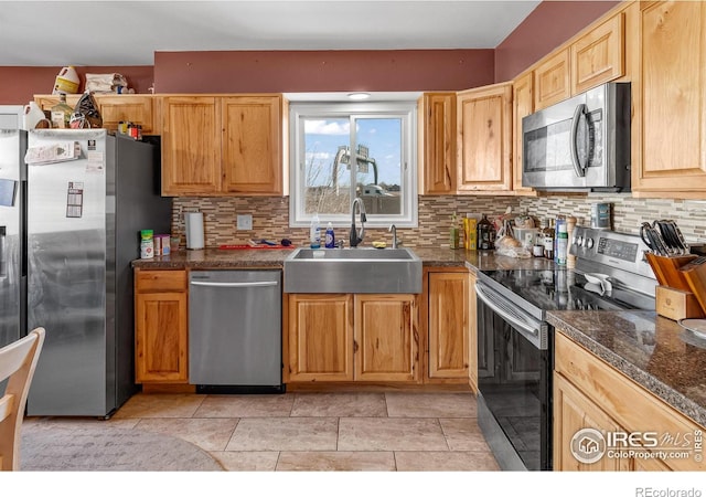 kitchen featuring appliances with stainless steel finishes, sink, decorative backsplash, and dark stone counters