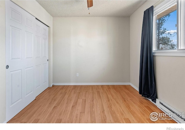 unfurnished bedroom featuring ceiling fan, a baseboard heating unit, light hardwood / wood-style flooring, and a textured ceiling