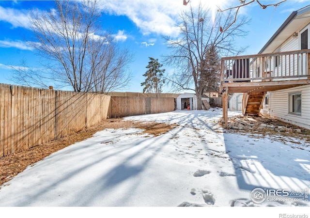 snowy yard featuring a storage shed and a wooden deck