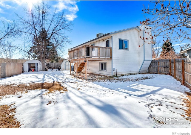 snow covered back of property featuring a shed and a deck