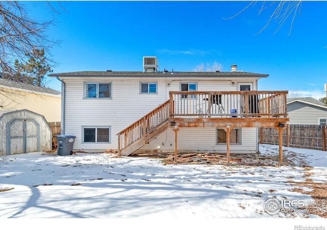 snow covered house with a storage shed, central AC, and a deck