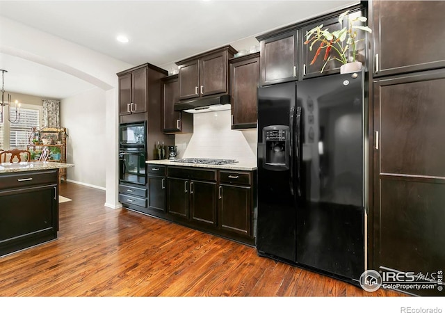 kitchen with dark wood-type flooring, hanging light fixtures, dark brown cabinets, black appliances, and decorative backsplash