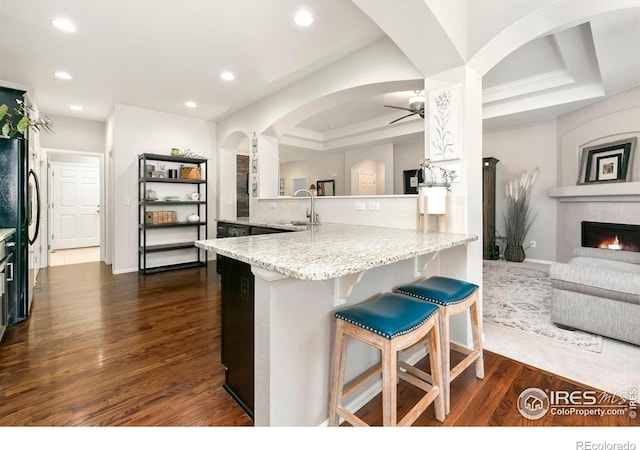 kitchen featuring sink, a kitchen bar, light stone countertops, black fridge, and kitchen peninsula