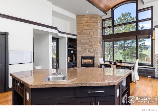 kitchen featuring sink, light hardwood / wood-style flooring, a high ceiling, a center island with sink, and a stone fireplace