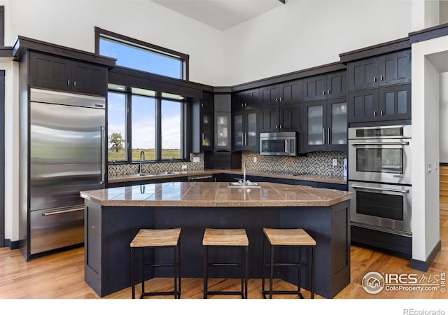 kitchen with a breakfast bar, sink, a center island with sink, stainless steel appliances, and backsplash