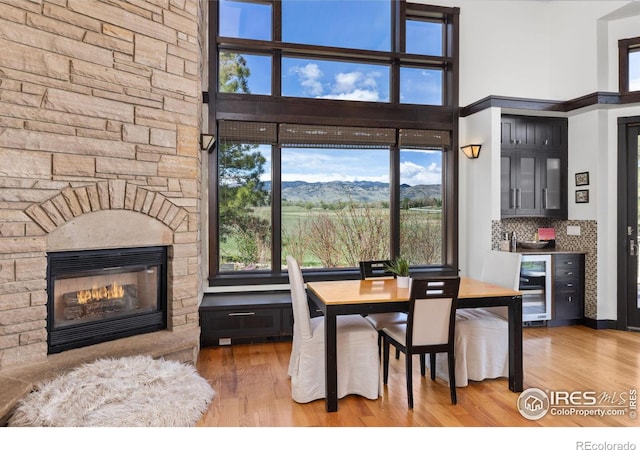 dining space featuring wood-type flooring, beverage cooler, a mountain view, and a stone fireplace