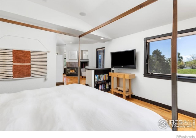 bedroom featuring a fireplace, hardwood / wood-style flooring, and vaulted ceiling