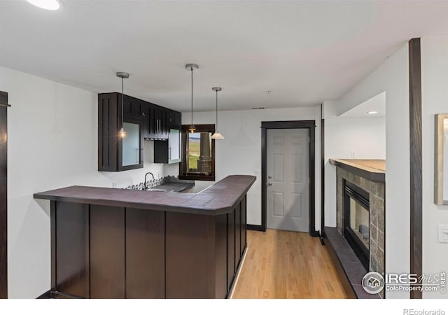 kitchen featuring dark brown cabinetry, hanging light fixtures, light hardwood / wood-style flooring, and kitchen peninsula