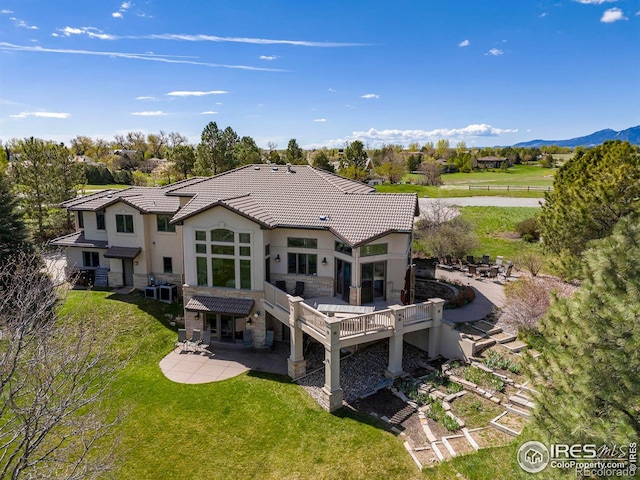 rear view of house featuring a deck with mountain view, a lawn, and a patio area