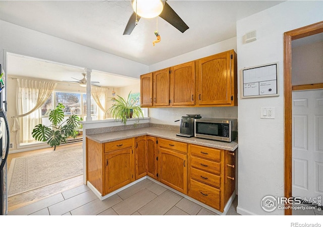 kitchen with light countertops, stainless steel microwave, brown cabinetry, ceiling fan, and a peninsula